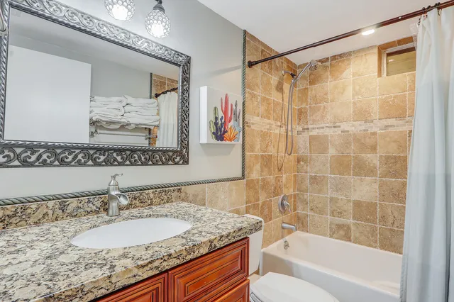 a bathroom with a granite countertop sink a mirror a bathtub and shower