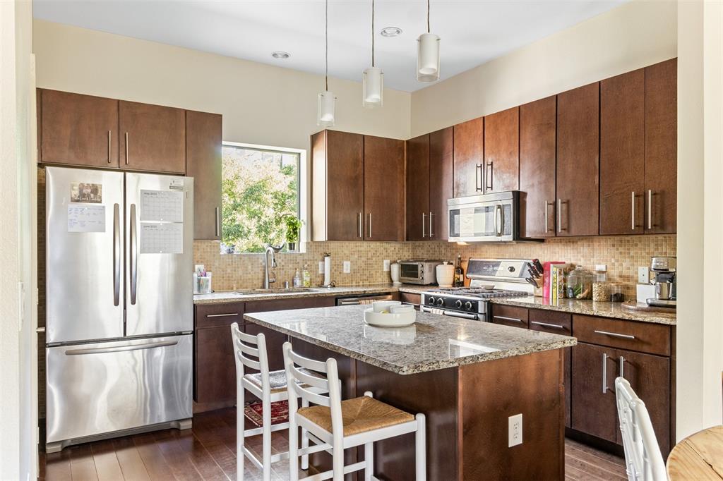 a kitchen with stainless steel appliances granite countertop a refrigerator a sink a stove a dining table and chairs