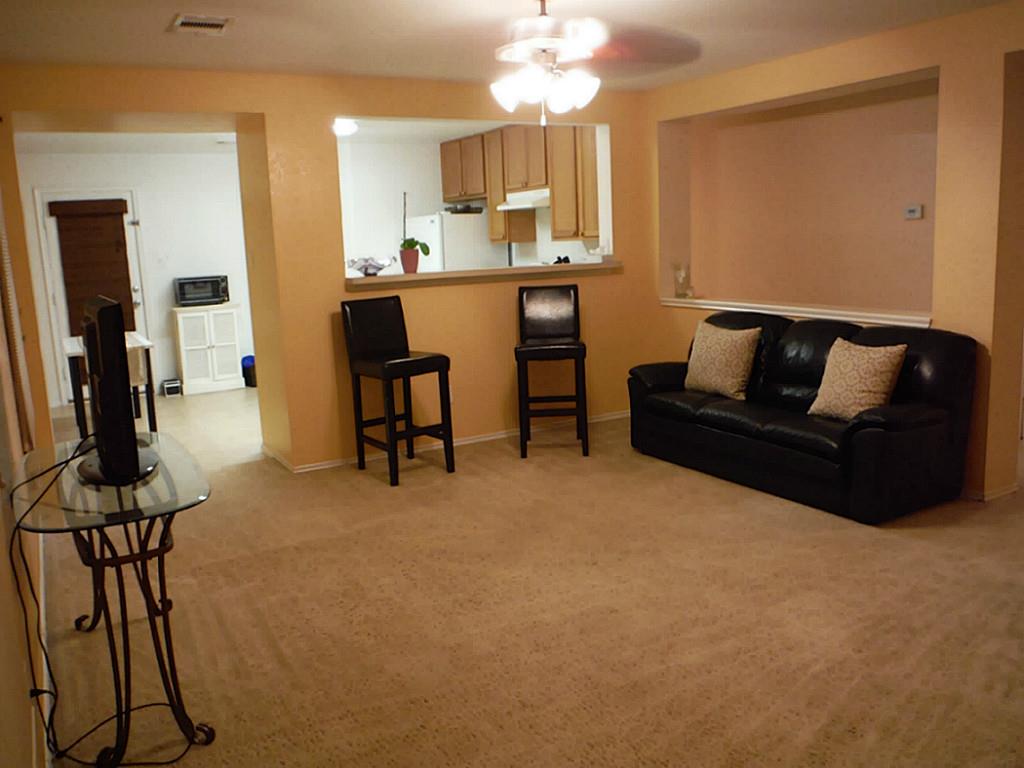 3142 Aspen Fair Trail Spring, TX 77389 - Photo 7 of 22 This photo shows a cozy living room with beige carpet and walls. There's an open view into the kitchen with a bar. The space appears warm and inviting, suitable for relaxation and entertaining.