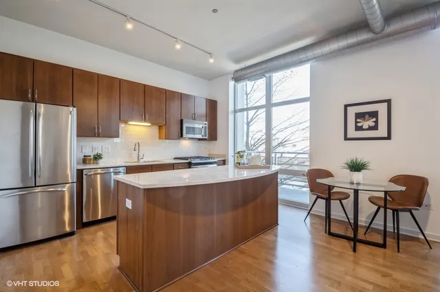 a kitchen with stainless steel appliances granite countertop a stove a refrigerator a sink a dining table and chairs with wooden floor