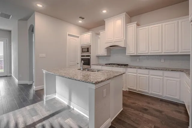 a kitchen with granite countertop a sink stainless steel appliances white cabinets and wooden floor