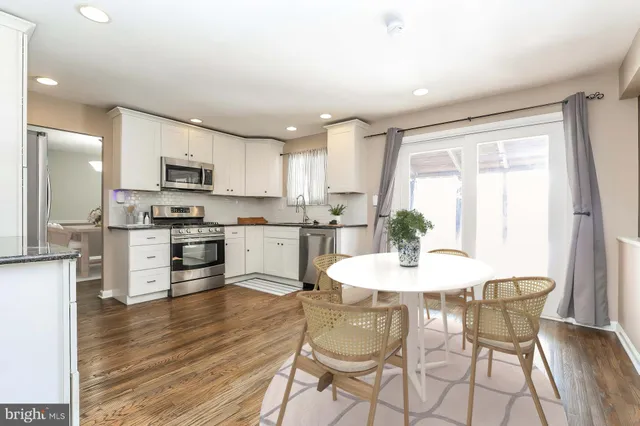 a kitchen with stainless steel appliances white cabinets a sink a stove a refrigerator and microwave with wooden floor