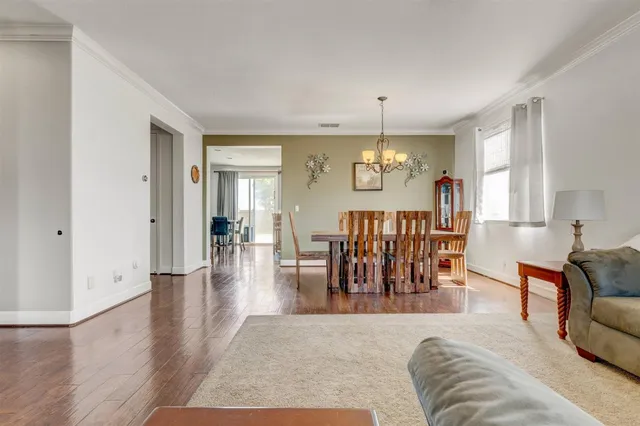 a living room with couches chandelier and a dining table with wooden floor