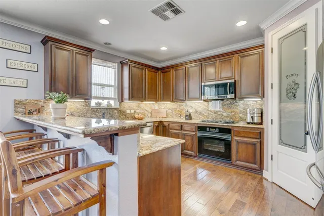 a kitchen with stainless steel appliances granite countertop a stove top oven a sink dishwasher a dining table and chairs with wooden floor