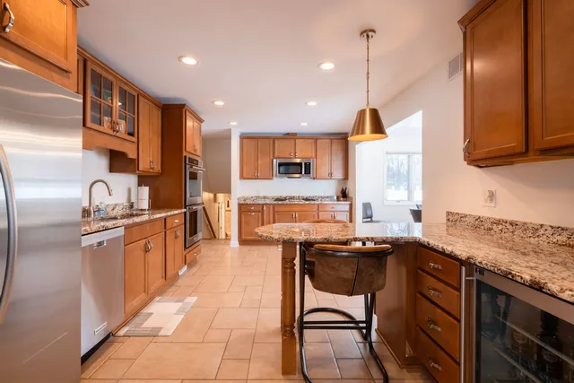 a kitchen with stainless steel appliances granite countertop a sink a stove a refrigerator cabinets and chairs