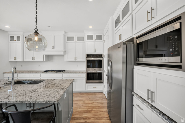 6536 West Muirfield Road Highland, UT 84003 - Photo 8 of 48 Gourmet kitchen featuring a large island with an undermount sink, white shaker cabinetry, stainless steel appliances, and wood-finish flooring