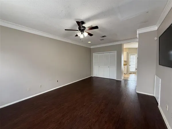 a view of an empty room with wooden floor and a ceiling fan