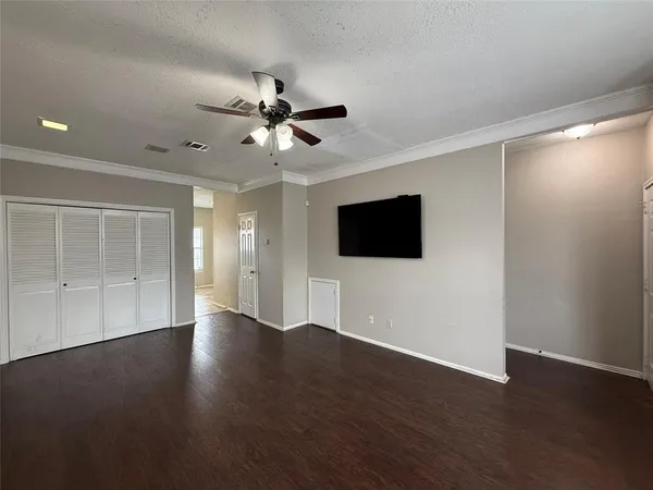 a view of an empty room with wooden floor and a ceiling fan