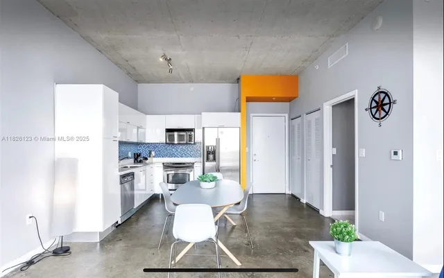 a living room with stainless steel appliances furniture a rug and a kitchen view