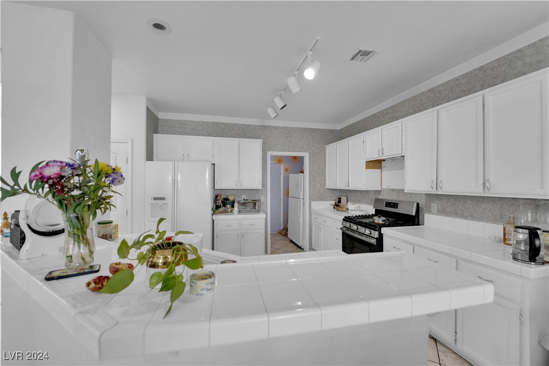 5790 Native Dancer Court Las Vegas, NV 89113 - Photo 5 of 26 Kitchen featuring stainless steel gas stove, white refrigerator with ice dispenser, wallpapered walls, white cabinets, and freestanding refrigerator