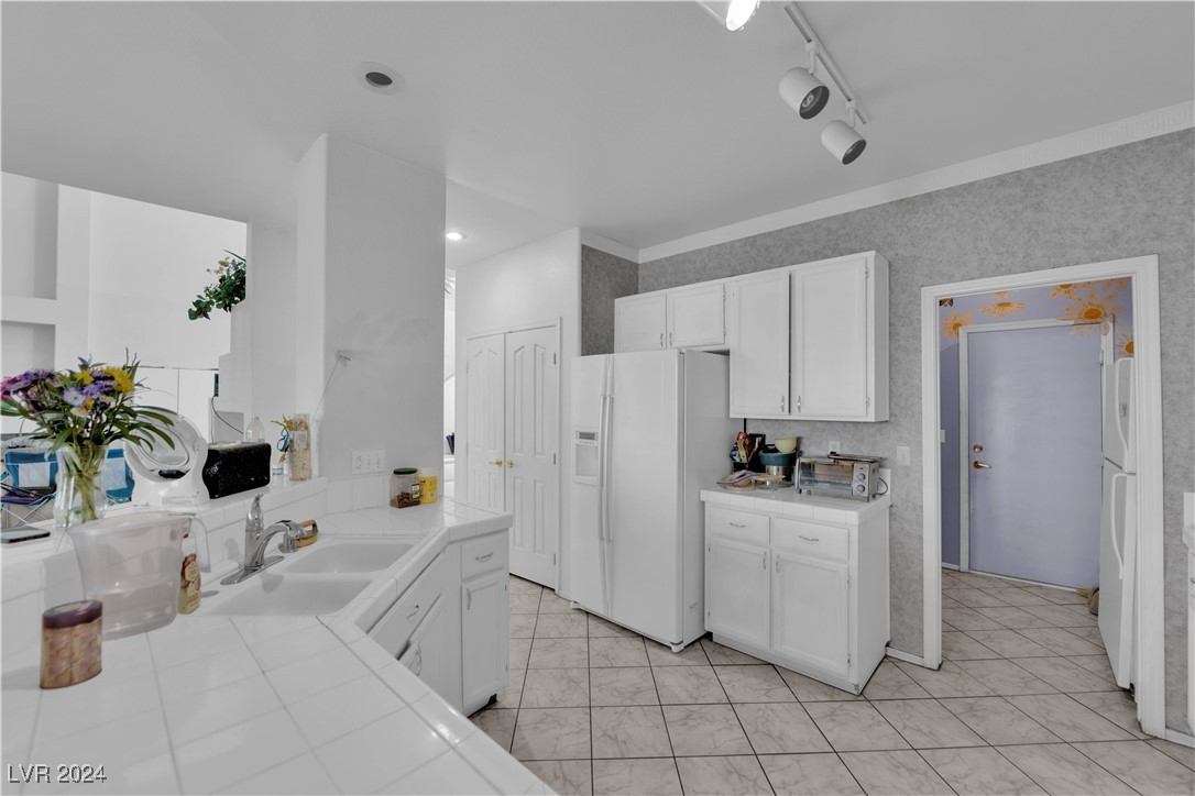 5790 Native Dancer Court Las Vegas, NV 89113 - Photo 6 of 26 Kitchen with white cabinets, tile countertops, white fridge with ice dispenser, rail lighting, and freestanding refrigerator