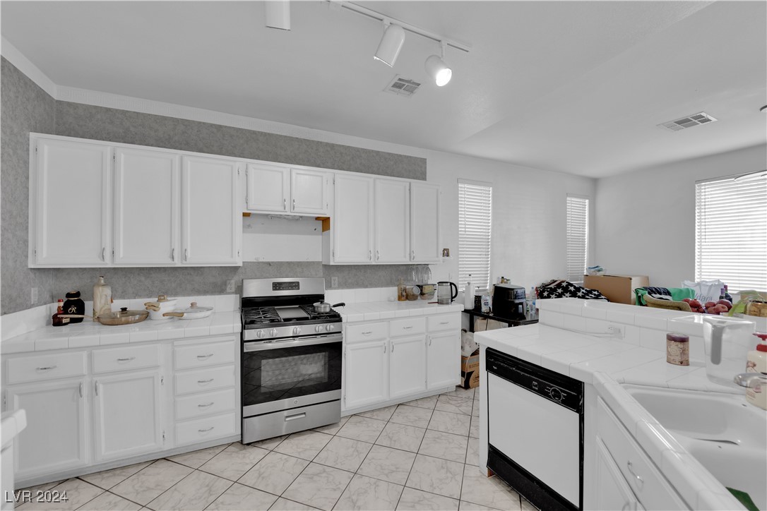 5790 Native Dancer Court Las Vegas, NV 89113 - Photo 7 of 26 Kitchen with tile counters, stainless steel range with gas cooktop, white cabinetry, white dishwasher, and track lighting