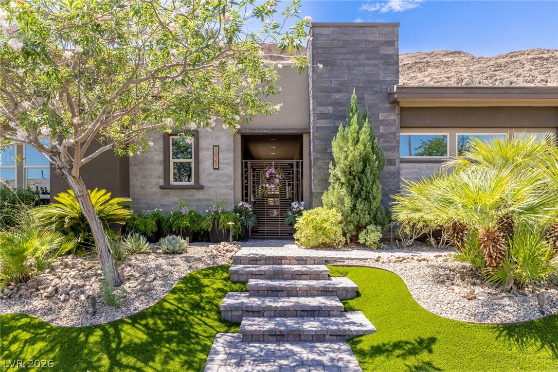 A striking modern facade welcomes with tiered stone steps, lush xeriscape, and vibrant green artificial turf leading to the entry.
