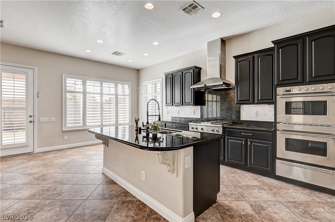 2793 Rosenhearty Drive Henderson, NV 89044 - Photo 7 of 85 This kitchen showcases a central island with a sink, elegant dark cabinetry, and integrated stainless steel appliances.