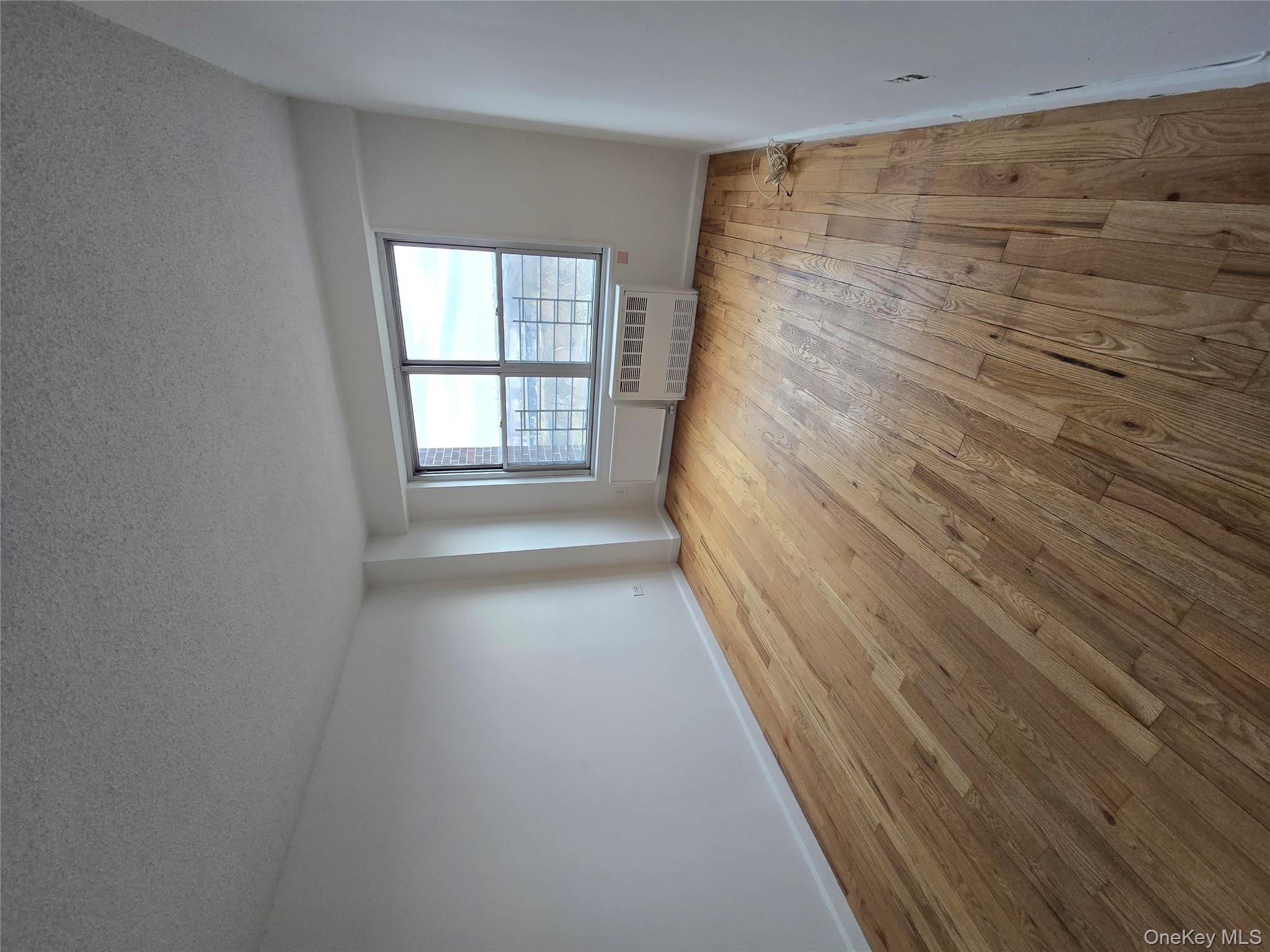 34-12 113th Street, Unit 8G Queens, NY 11368 - Photo 4 of 13 wooden floor in an empty room with a window
