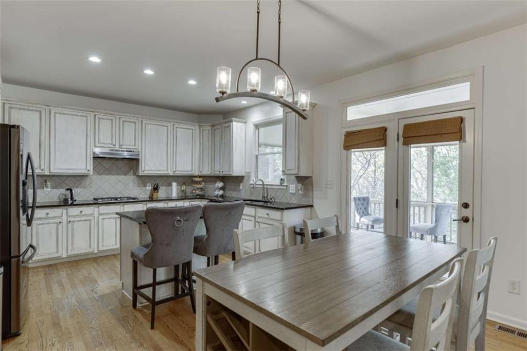 4880 Stone Moss Path Hoschton, GA 30548 - Photo 12 of 66 a kitchen with stainless steel appliances granite countertop a stove a refrigerator a sink a dining table and chairs with wooden floor