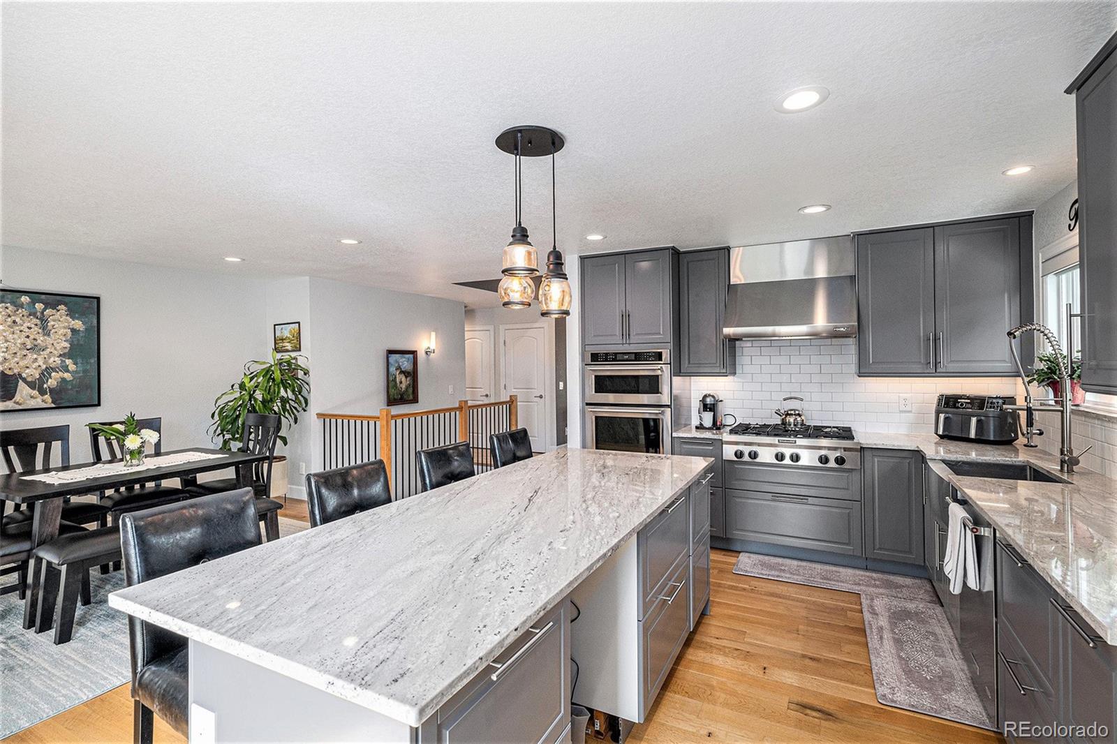 904 Fieldstone Place Highlands Ranch, CO 80126 - Photo 9 of 28 a large kitchen with stainless steel appliances kitchen island granite countertop a large kitchen island a stove a refrigerator a sink a dining table and chairs with wooden floor