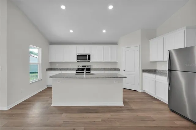 a kitchen with stainless steel appliances a refrigerator a stove a sink dishwasher and white cabinets with wooden floor