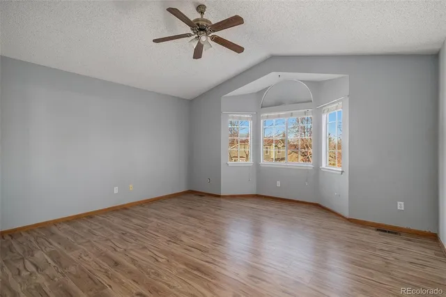 an empty room with wooden floor chandelier fan and windows
