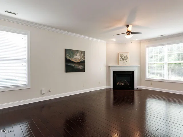 an empty room with wooden floor fireplace and windows