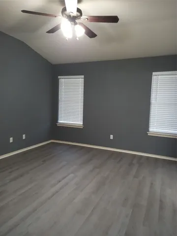 an empty room with wooden floor chandelier fan and windows