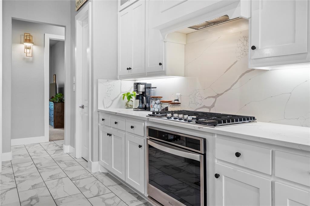 1024 Henry Way Springtown, TX 76082 - Photo 11 of 29 Gourmet kitchen featuring a stainless steel gas cooktop and oven, white cabinetry with black hardware, under-cabinet lighting, and a patterned backsplash extending to the countertop
