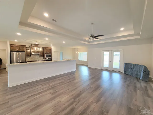 a view of an empty room and kitchen with wooden floor