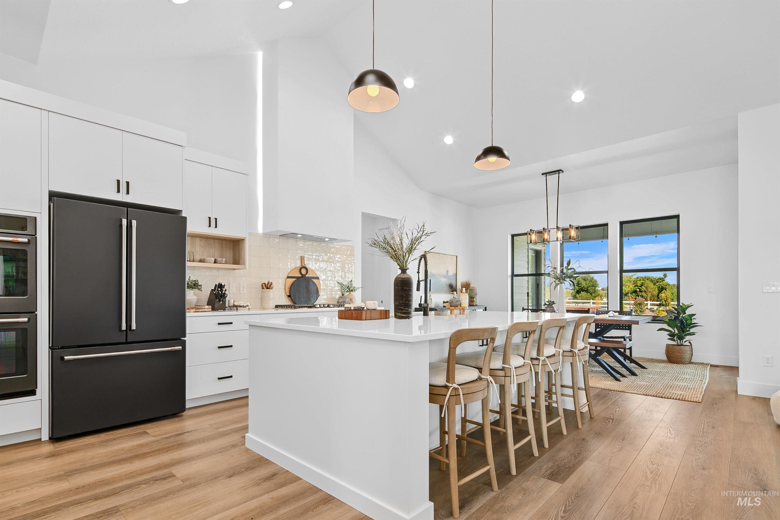 23910 Timber Hls Road Caldwell, ID 83607 - Photo 15 of 50 Kitchen featuring high end black refrigerator, high vaulted ceiling, hanging light fixtures, white cabinets, and light wood-style flooring