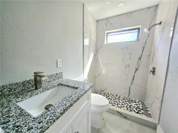 a bathroom with a granite countertop sink a toilet and shower