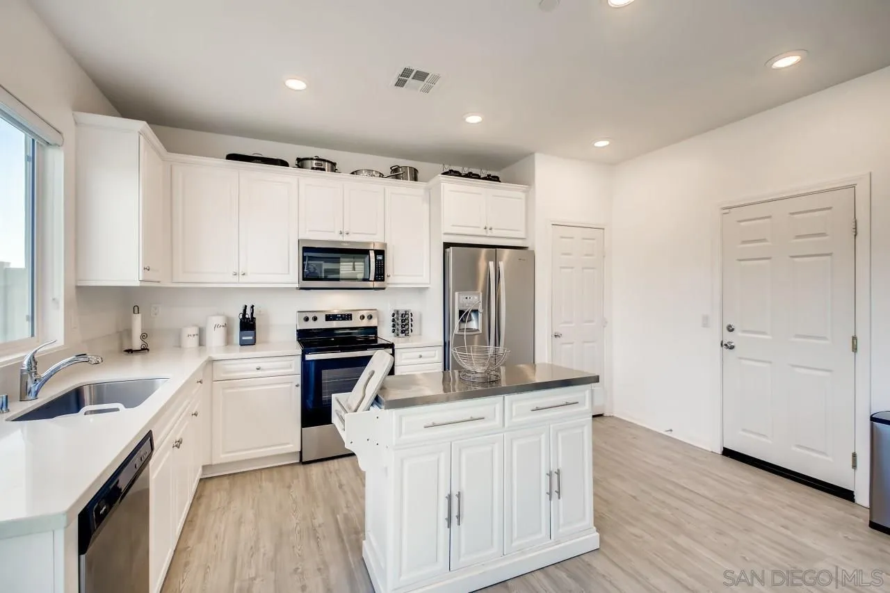 10633 Busch Street Spring Valley, CA 91978 - Photo 11 of 28 a kitchen with stainless steel appliances granite countertop a refrigerator oven a sink dishwasher and white cabinets with wooden floor