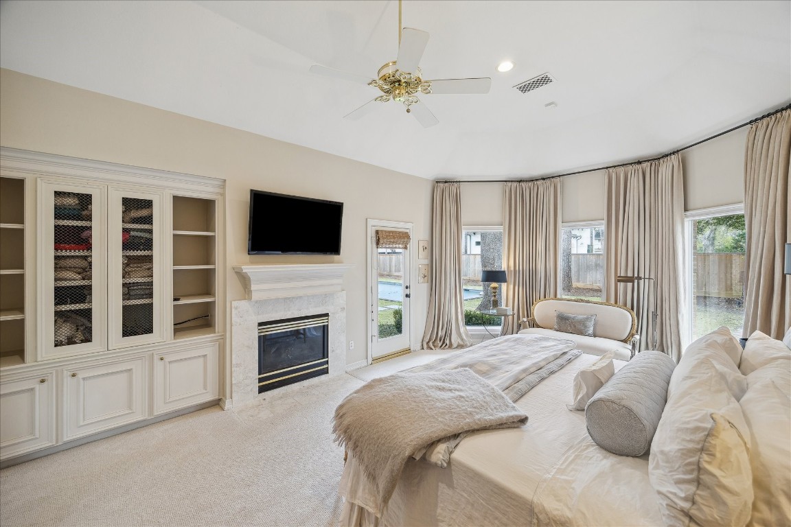 11524 Taylorcrest Road Houston, TX 77024 - Photo 27 of 47 The primary bedroom features large windows and a patio door opening to the covered back patio, backyard, and pool. Additional highlights include a gas log fireplace, tray ceiling, built-in cabinets with shelving and metal door fronts, ceiling fan, a dedicated AC and heat thermostat, and an alarm wall monitor.