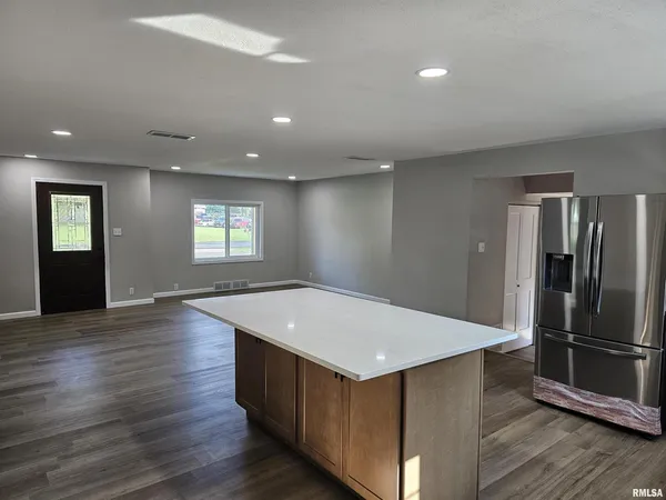 an empty room with wooden floor kitchen view and windows
