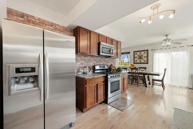 a kitchen with stainless steel appliances granite countertop a refrigerator a stove a sink a dining table and chairs with wooden floor