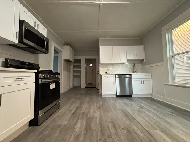 a kitchen with stainless steel appliances a stove a sink and white cabinets with wooden floor