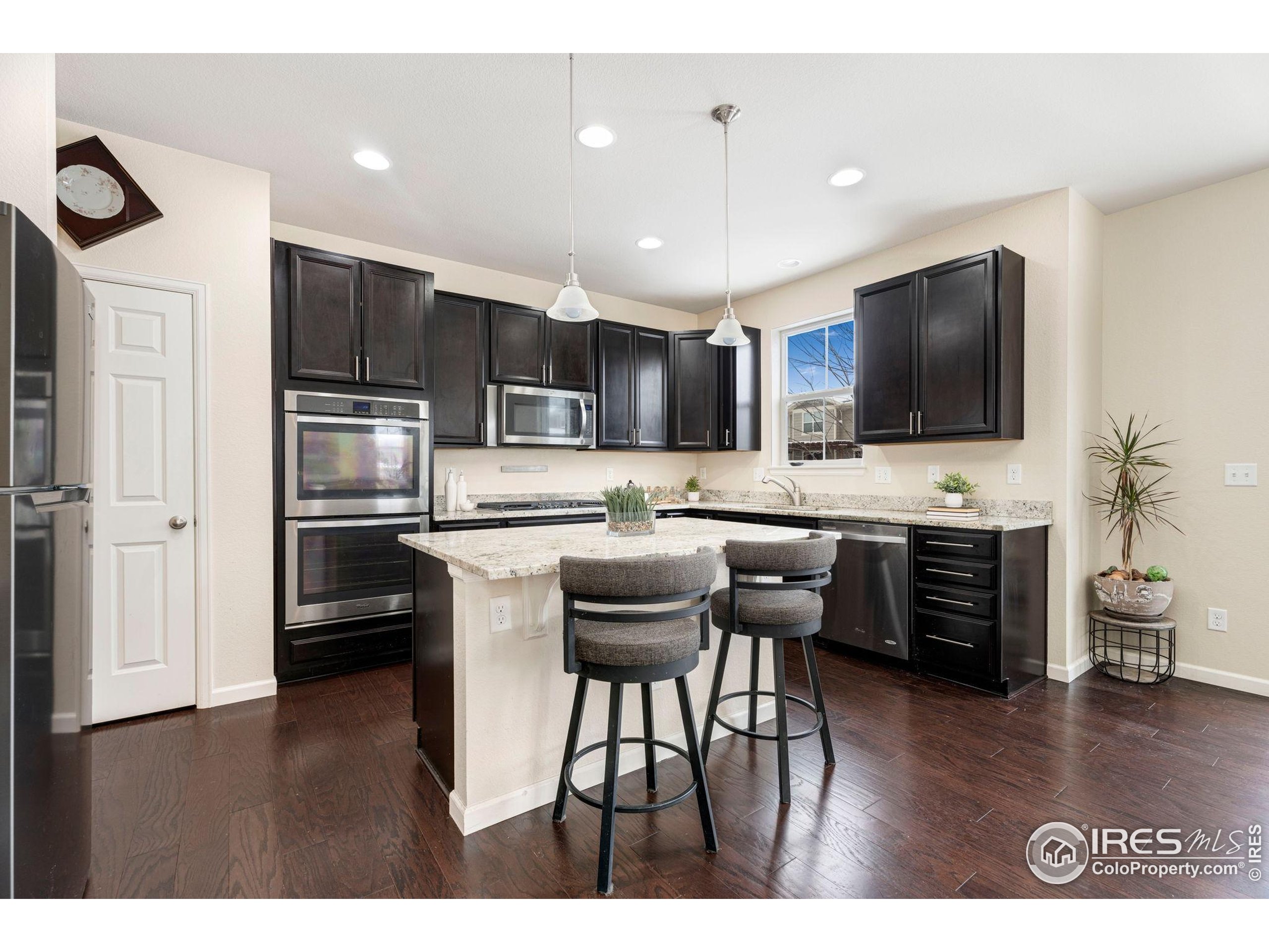 6770 Spring Rain Road Timnath, CO 80547 - Photo 12 of 30 a kitchen with stainless steel appliances kitchen island granite countertop a refrigerator a stove a sink dishwasher a dining table and chairs with wooden floor