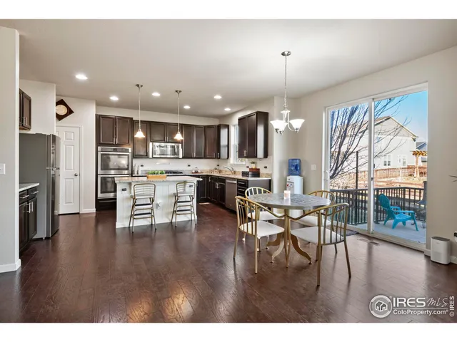 a open kitchen with stainless steel appliances granite countertop a stove top oven a refrigerator a dining table and chairs with wooden floor