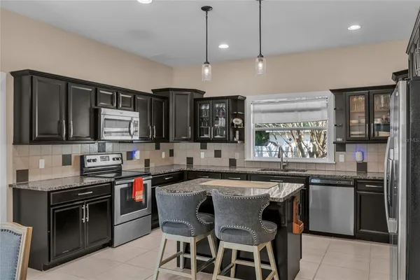 a kitchen with stainless steel appliances granite countertop a sink a stove a refrigerator and chairs
