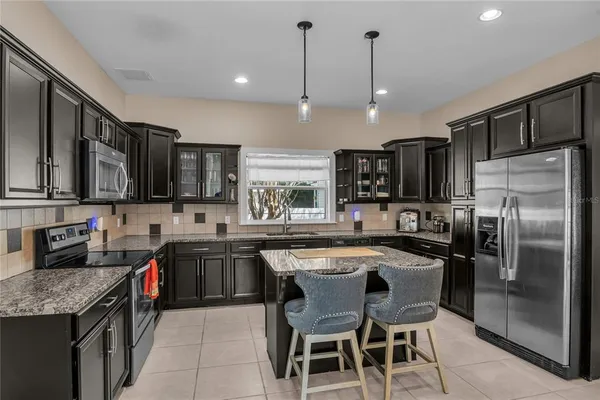 a kitchen with stainless steel appliances granite countertop a sink a stove a refrigerator and chairs