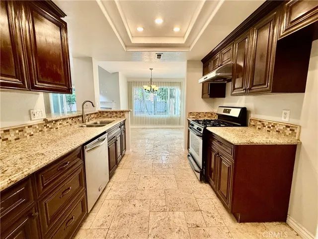 a kitchen with stainless steel appliances granite countertop stove top oven a sink dishwasher and wooden cabinets with wooden floor