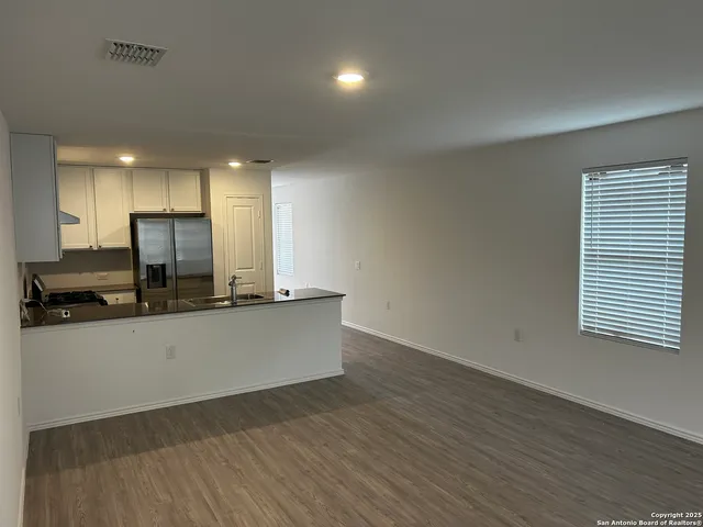 a living room with stainless steel appliances wooden floors and kitchen view