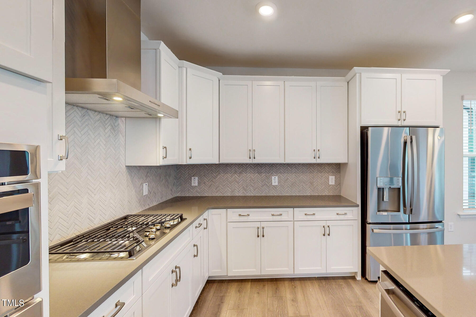 2403 Greshford Lane Raleigh, NC 27615 - Photo 5 of 35 Gourmet kitchen with white cabinets, grey herringbone backsplash and stainless steel appliances.