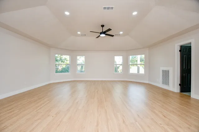 an empty room with wooden floor ceiling fan and windows