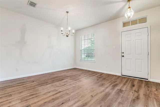 an empty room with wooden floor chandelier and windows