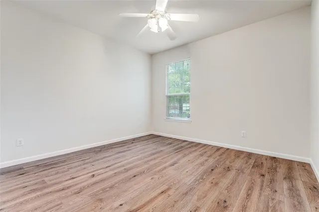 an empty room with wooden floor chandelier fan and windows