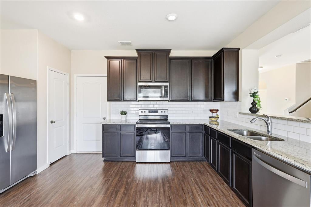 227 Curt Street Anna, TX 75409 - Photo 10 of 40 Kitchen with light stone countertops, appliances with stainless steel finishes, dark wood finished floors, and tasteful backsplash