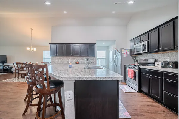 a kitchen with stainless steel appliances granite countertop a table chairs sink and cabinets