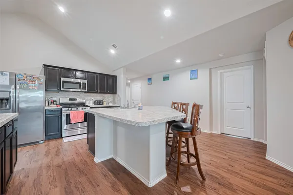 a kitchen with stainless steel appliances kitchen island granite countertop a stove a refrigerator a sink a dining table and chairs with wooden floor