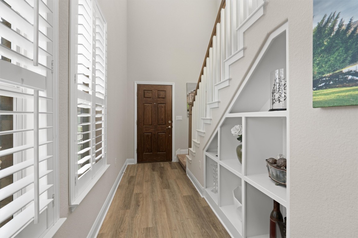 10502 Turnbull Loop, Unit 41 Austin, TX 78717 - Photo 3 of 29 Light-filled entry showcasing LVP flooring, custom built-in shelving, plantation shutters, and an open staircase with white railing.
