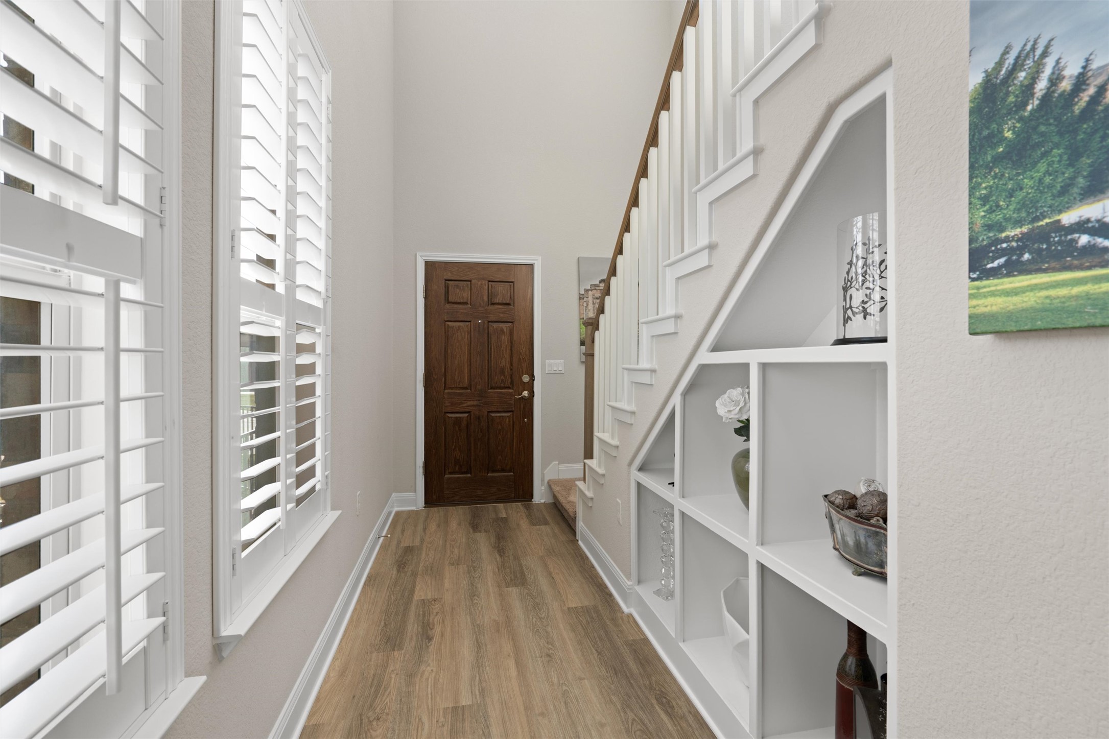 10502 Turnbull Loop, Unit 41 Austin, TX 78717 - Photo 4 of 35 Light-filled entry showcasing LVP flooring, custom built-in shelving, plantation shutters, and an open staircase with white railing.