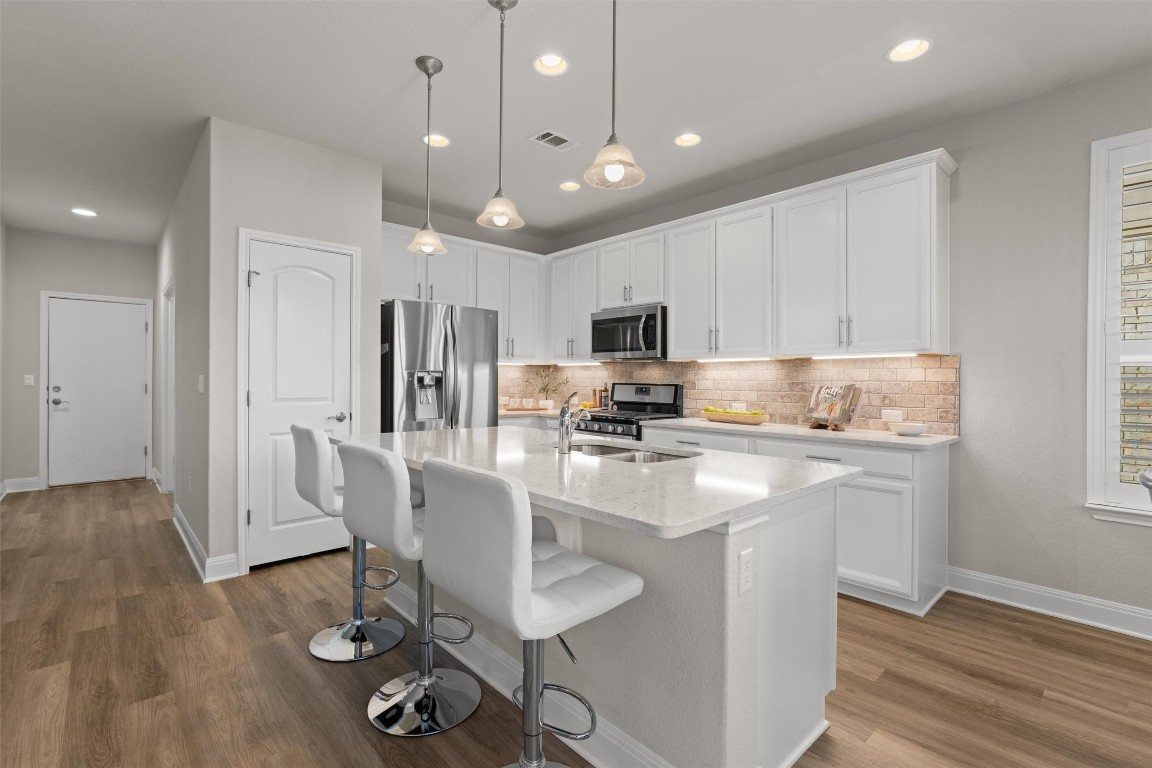 10502 Turnbull Loop, Unit 41 Austin, TX 78717 - Photo 7 of 29 Bright and open kitchen featuring stainless steel appliances, a spacious center island with sink, granite countertops, breakfast bar seating, under-cabinet lighting, and elegant white cabinetry.